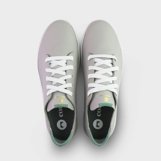 
                      
                        A top view shot of pair of light grey leather sneakers with a lace-up closure featuring flat white shoelaces, gold printing on the tongue and a dark grey sockliner with a circle logo and COMUNITY printed in white with a green heel accent.
                      
                    