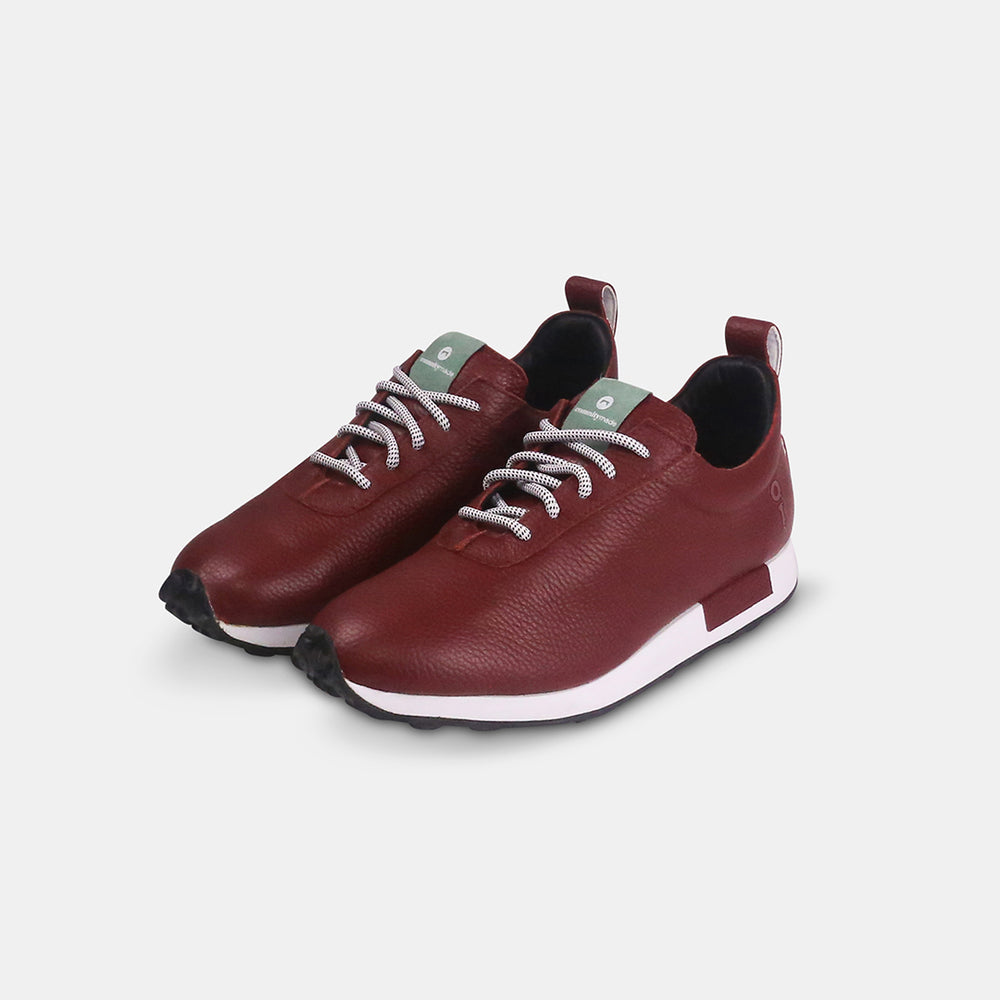A pair of burgundy-colored leather golf sneakers with white soles and black laces with white flecks. The shoes have a small mint green accent on the tongue and a burgundy leather pull tab on the back.