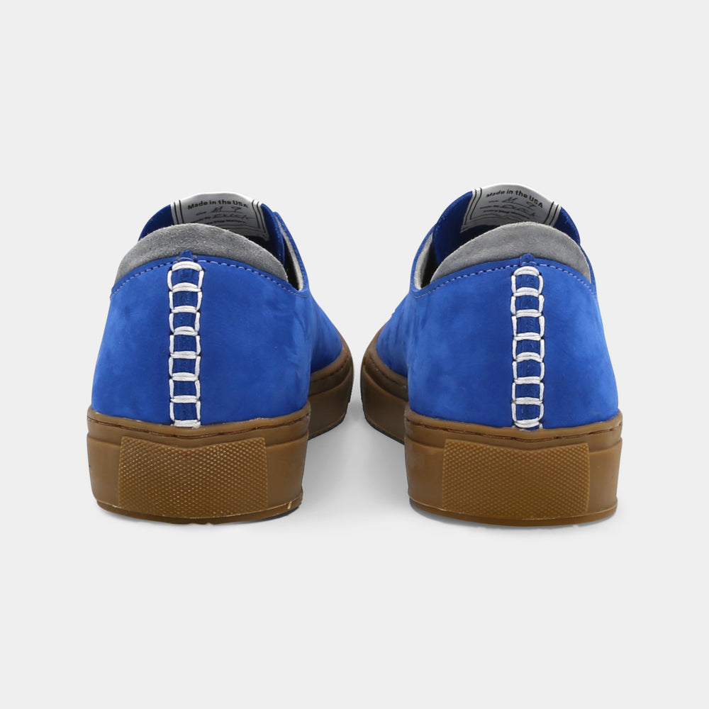 
                      
                        A blue low-top sneaker with a brown sole and laces, back view.
                      
                    