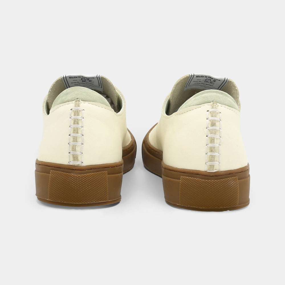
                      
                        A latte colored low-top sneaker with a brown sole and white laces, back view.
                      
                    