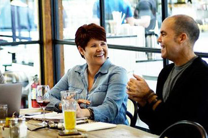 Picture of a man and a woman sitting in a restaurant looking at each other smiling. These are the founders of COMUNITYmade.