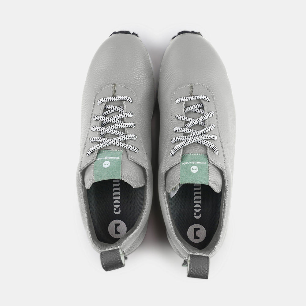 
                      
                        A pair of gray sneakers with a subtle grainy texture and white soles. A small mint green tag is at the base of the heel, just above the sole. A small white text logo is printed vertically on the back of each shoe.
                      
                    