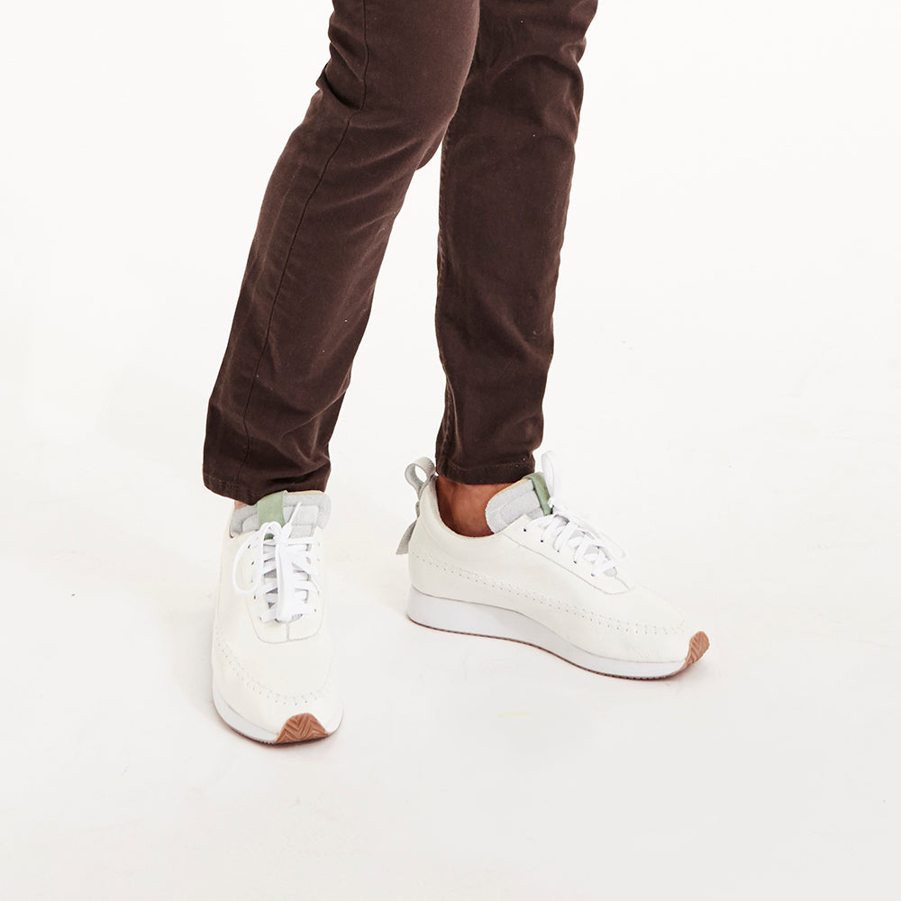 
                      
                        A picture from the waist down of a man with burgundy pants wearing a pair of White lace up COMUNITYmade Traction shoes. The shoes have white accent stitching and a gum rubber herringbone outsole
                      
                    