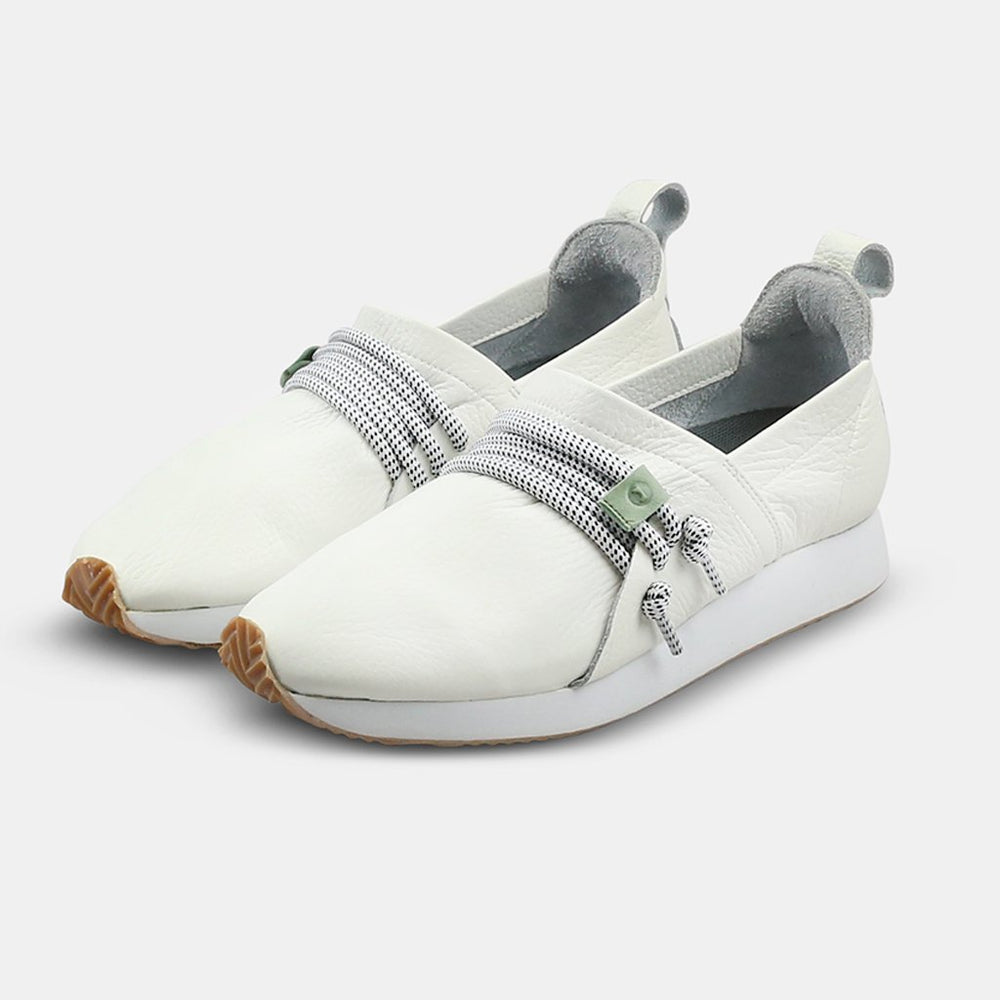 
                      
                        A three-quarter, low-angle view of two white Comunitymade slip-on shoes. The shoes are made of a white, pebbled leather and have a chunky white sole with a gum-colored accent at the toe. Thick gray and white speckled laces wrap around the top of the shoe, held in place by a mint green lace lock.
                      
                    