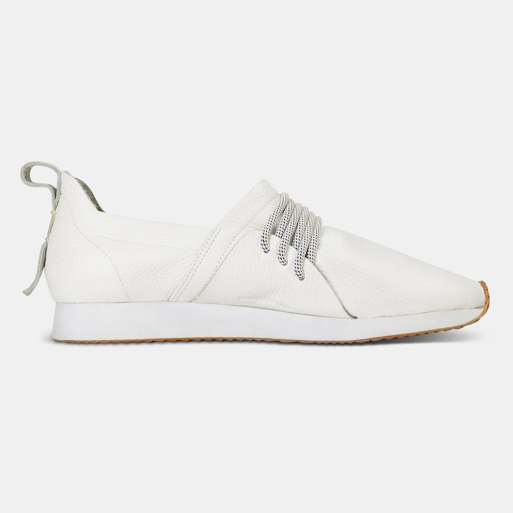 
                      
                        A side profile of a single white Comunitymade slip-on shoe. The shoe is made of a white, pebbled leather with thick gray and white speckled laces at the top. It has a flat white sole with a gum-colored accent at the toe.
                      
                    