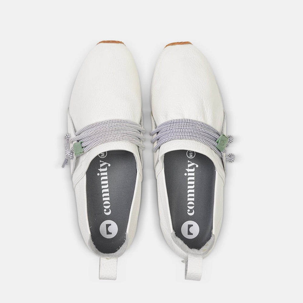 
                      
                        A top-down view of two white Comunitymade slip-on shoes. The shoes are made of a white, pebbled leather with thick gray and white speckled laces that wrap around the top. The insoles are dark gray with "comunity" and the brand's logo in white lettering.
                      
                    