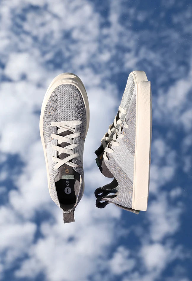 Grey and blue knit patterned sneakers shot on a cloud background that makes them look like they are floating in the air