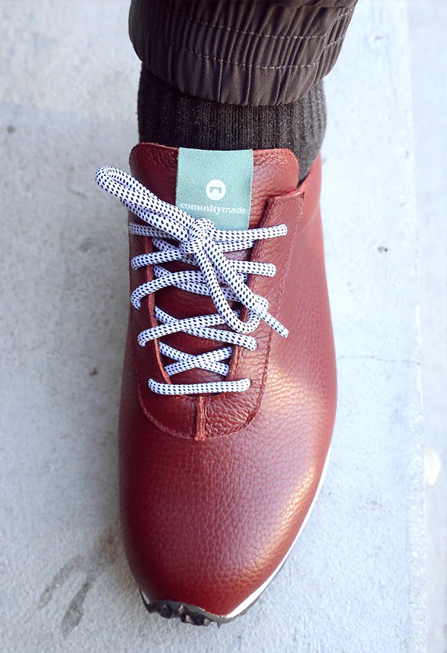 Top view of a burgundy leather shoe with round black and white shoe laces and a green accent color on the tongue
