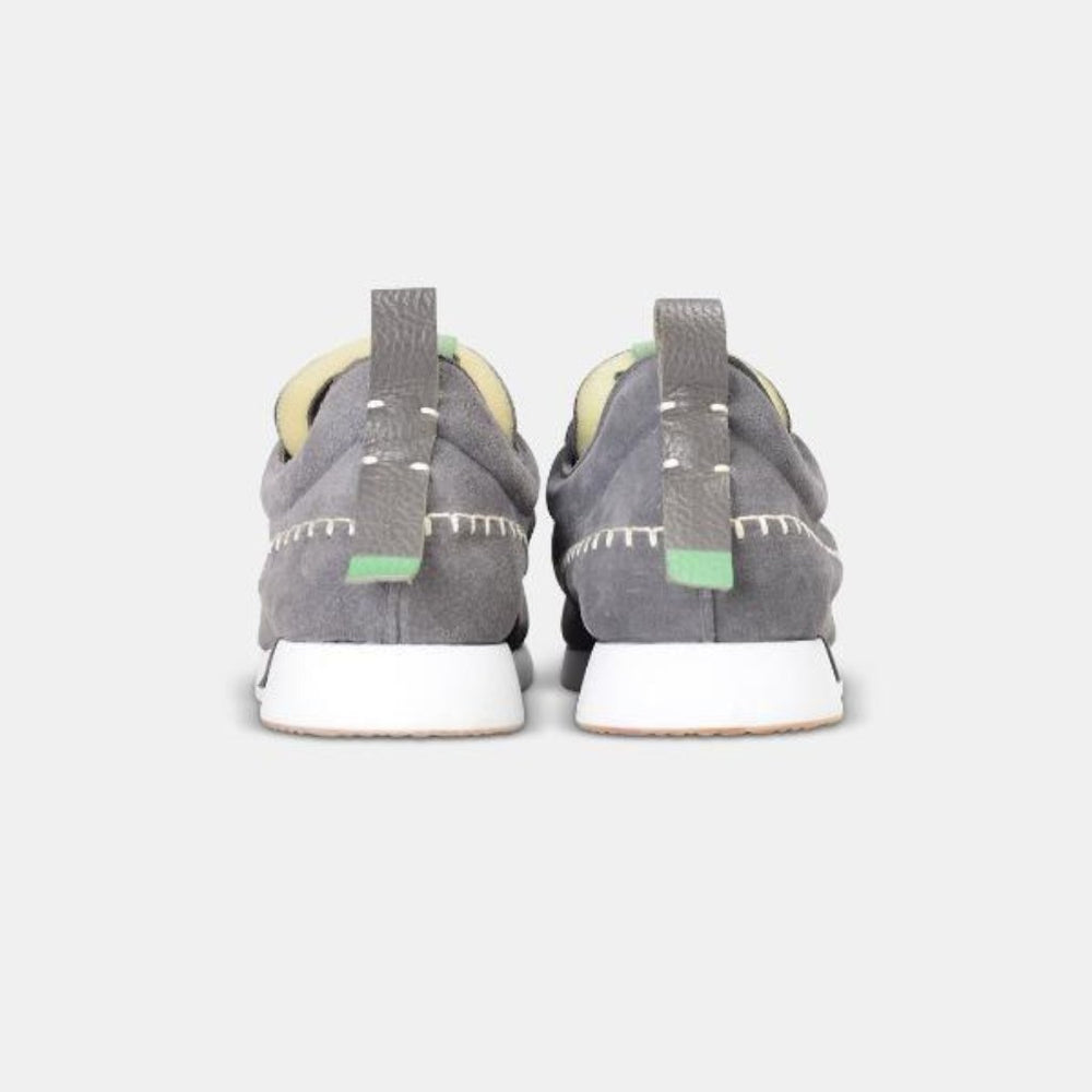
                      
                        A rear view picture of a pair of grey suede Comunitymade lace-up shoes. The shoe is made of a grey suede and has white accent stitching around the entire shoe, plus a grey heel pull tab with a light green accent.  The midsole is white with a gum rubber outsole.
                      
                    