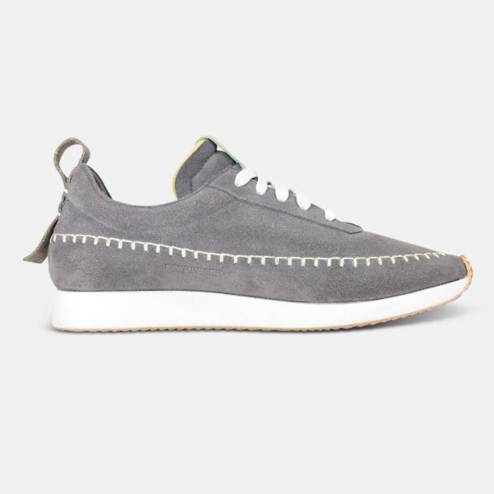 
                      
                        A side profile shot of a single grey Comunitymade lace-up shoe. The shoe is made of a grey suede, flat white laces and has white accent stitching around the entire shoe plus a grey heel pull tab. It has a flat white sole with a gum-rubber colored outsole.
                      
                    