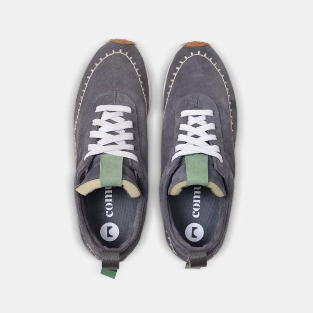 
                      
                        A top down view of a pair of grey suede Comunitymade lace-up shoes. The shoe is made of a grey suede and has a green tongue accent.  It has flat white laces and white accent stitching around the entire shoe plus a grey heel pull tab. The insole is dark grey and has a circle logo plus the word COMUNITY printed in white. 
                      
                    