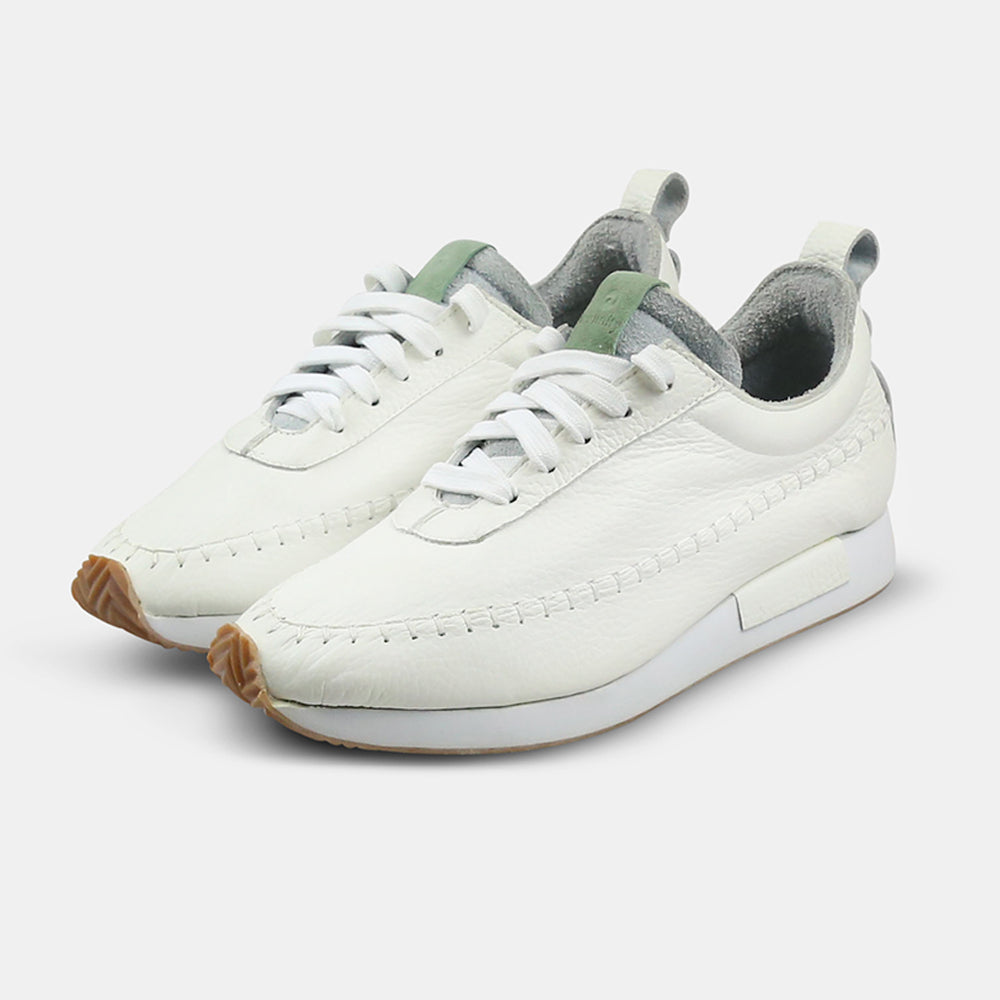 
                      
                        A quarter profile shot of a pair of white leather Comunitymade lace-up shoes. The shoe is made of a white leather with a green tongue accent.  It has flat white laces and white accent stitching around the entire shoe, plus a white heel pull tab. It has a flat white midsole with a gum-rubber colored outsole.
                      
                    