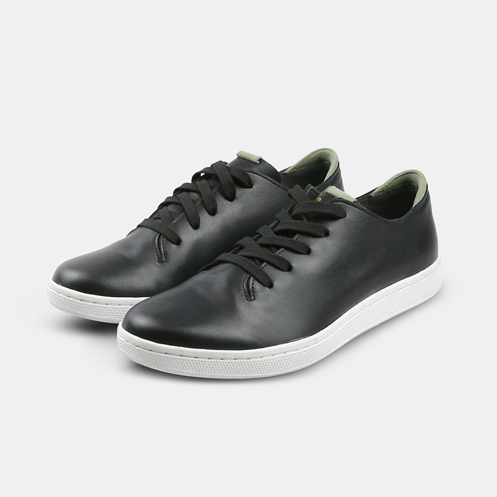 A quarter angle shot of pair of black leather sneakers with a lace-up closure featuring flat black shoelaces, a white rubber cupsole and a green accent on the heel.
