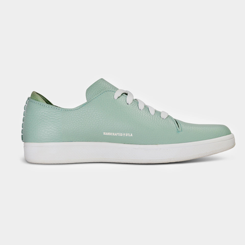 
                      
                        A medial profile shot of single light green leather sneaker with a lace-up closure, featuring flat white shoelaces, white accent stitching on the heel, white "Handcrafted in LA" printing on the instep and a white rubber cupsole.
                      
                    
