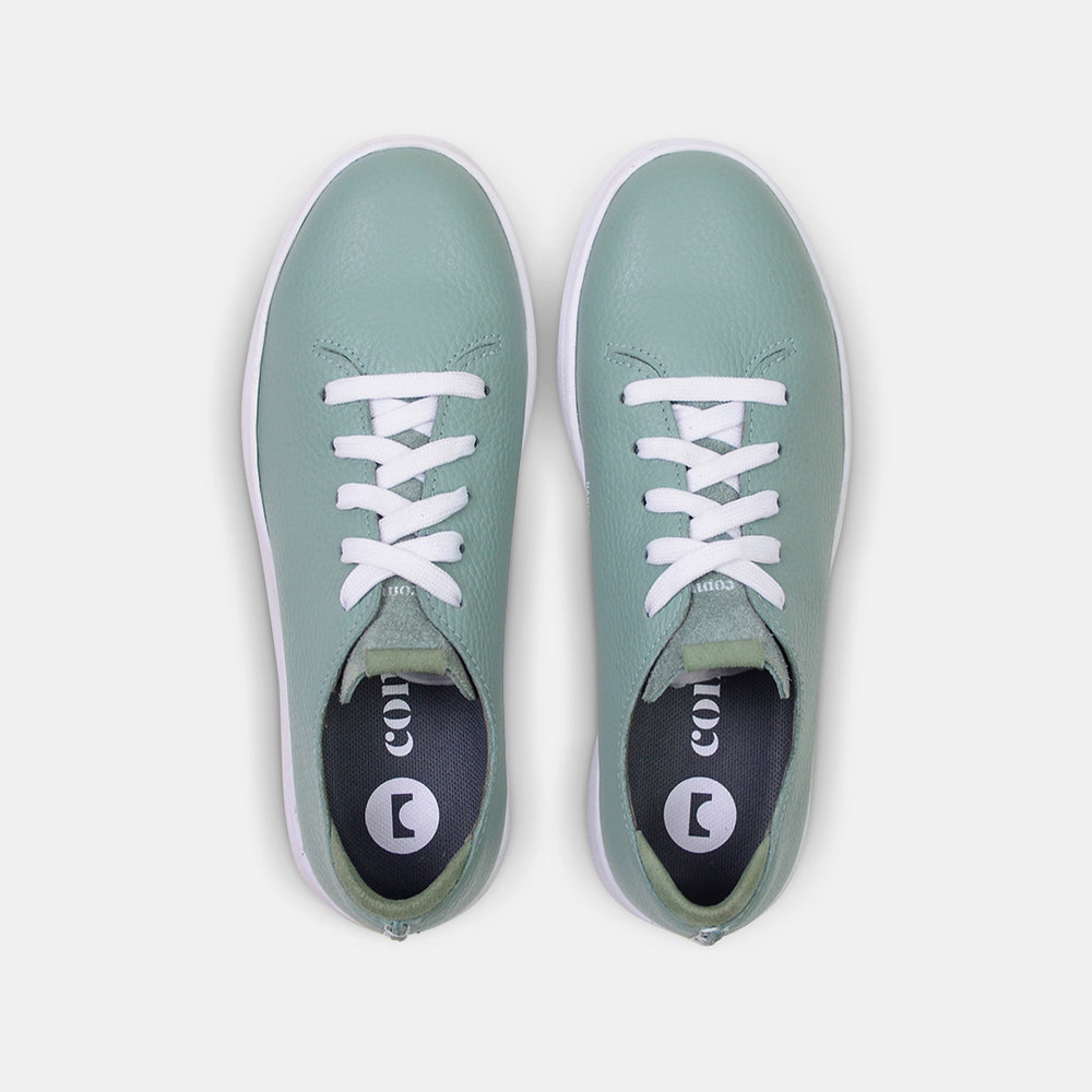 
                      
                        A top view shot of pair of light green leather sneakers with a lace-up closure featuring flat white shoelaces, white printing on the tongue and a dark grey sockliner with a circle logo and COMUNITY printed in white with a green heel accent.
                      
                    