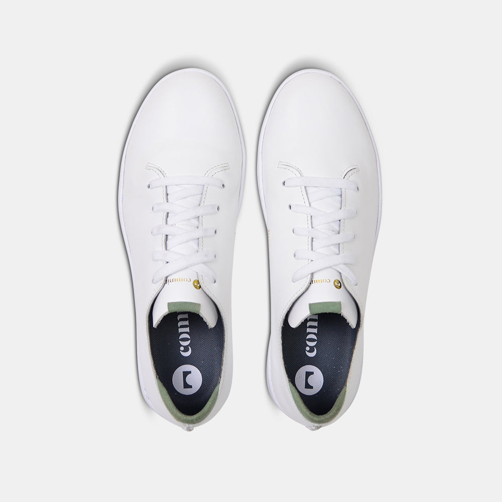 
                      
                        A top view shot of pair of white leather sneakers with a lace-up closure featuring flat white shoelaces, gold printing on the tongue and a dark grey sockliner with a circle logo and COMUNITY printed in white with a green heel accent.
                      
                    