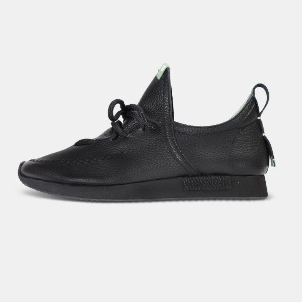 A single profile shot of a casual black leather mid-cut slip-on shoe with unique stitch detailing on the toe.  Round black laces with heel loop pull tab and a black midsole and black rubber outsole.