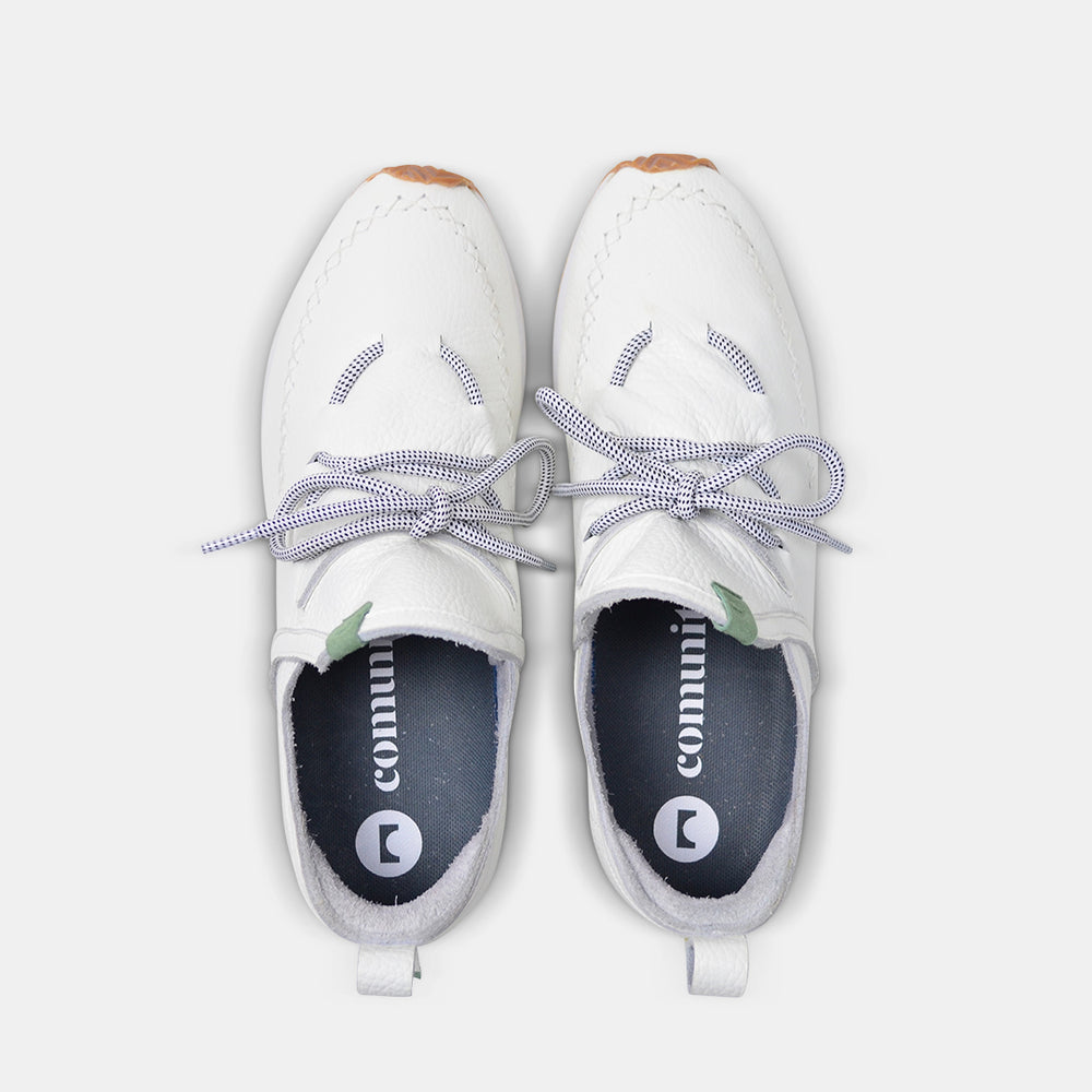 
                      
                        A top down view of a pair of casual white leather mid-cut slip-on shoe with unique stitch detailing on the toe and green branding accents.  Round white laces with heel loop pull tab. Insoles are dark grey with a round logo and COMUNITY printing in white.
                      
                    