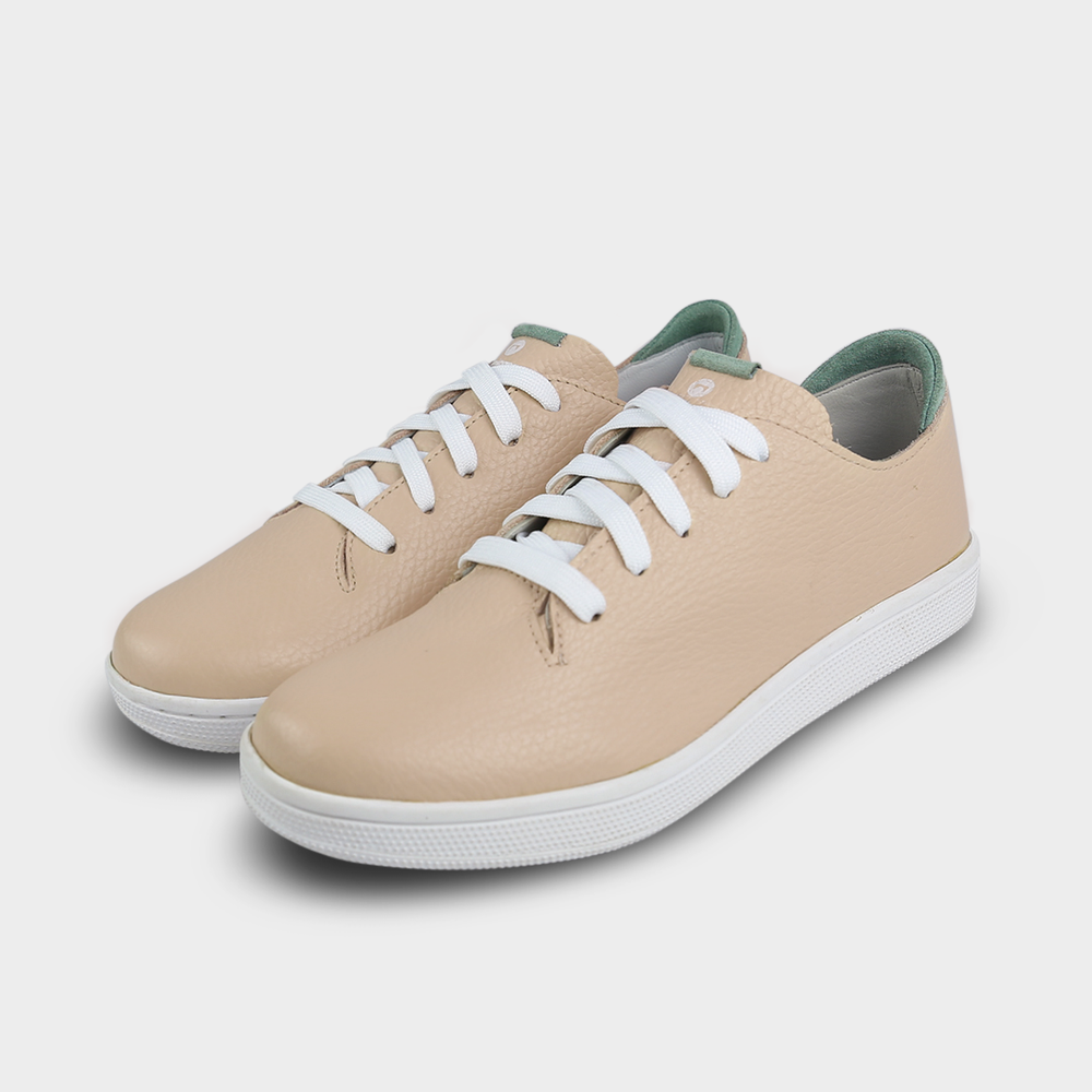
                      
                        A quarter angle shot of pair of nude beige leather sneakers with a lace-up closure featuring flat white shoelaces, a white rubber cupsole and a green accent on the heel.
                      
                    