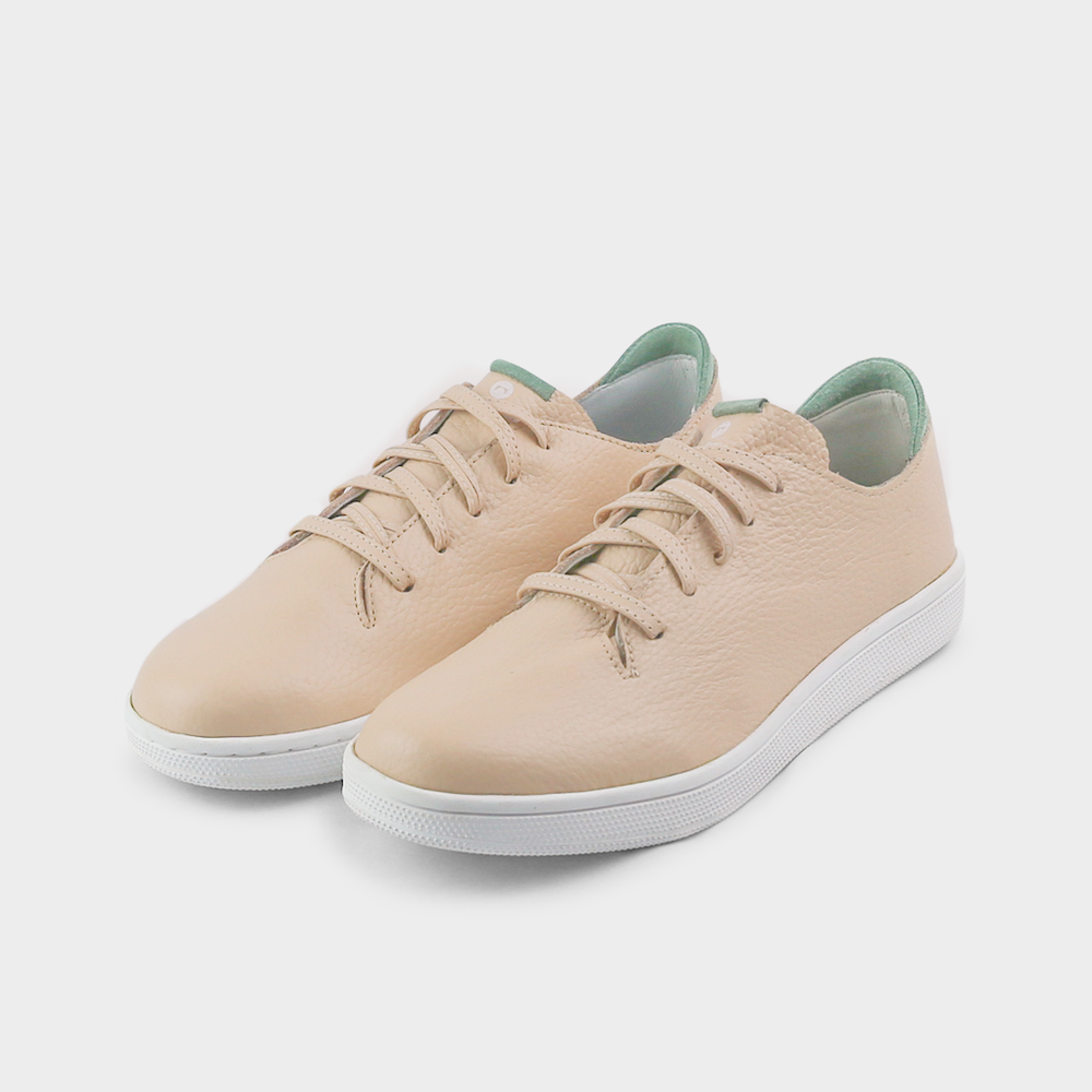 
                      
                        A quarter angle shot of pair of nude beige leather sneakers with a lace-up closure featuring flat nude beige leather shoelaces, a white rubber cupsole and a green accent on the heel.
                      
                    