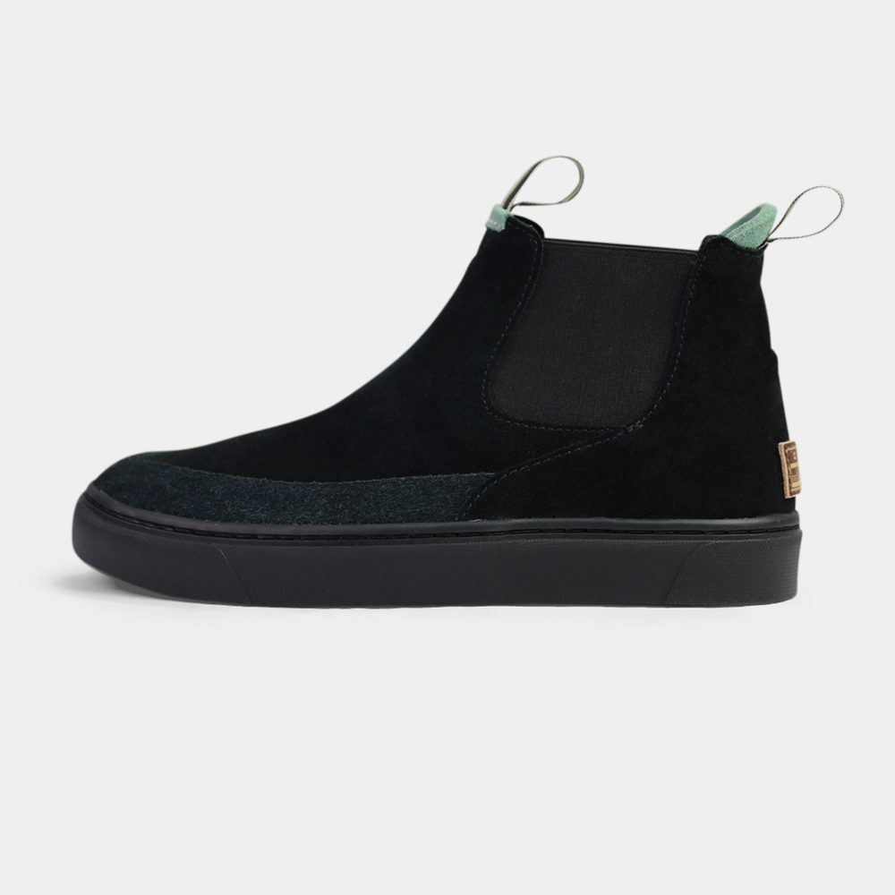 
                      
                        A side-shot of a pair of black suede boots. The shoes have black elastic gussets on the side and a striped pull tab at the heel. The black insoles feature a white "comunity" logo with a circle and an arrow.
                      
                    