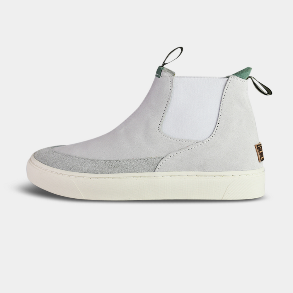 
                      
                        A pair of white suede boots with white soles. The boots feature a mint green elasticated panel and a striped brown and black pull tab at the back of the ankle. The toe area is a different texture of suede with a visible seam
                      
                    