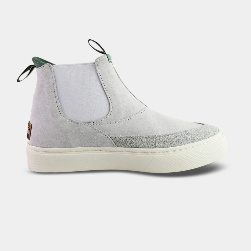 
                      
                        A pair of white suede boots with white soles. The boots feature a mint green elasticated panel and a striped brown and black pull tab at the back of the ankle. The toe area is a different texture of suede with a visible seam
                      
                    