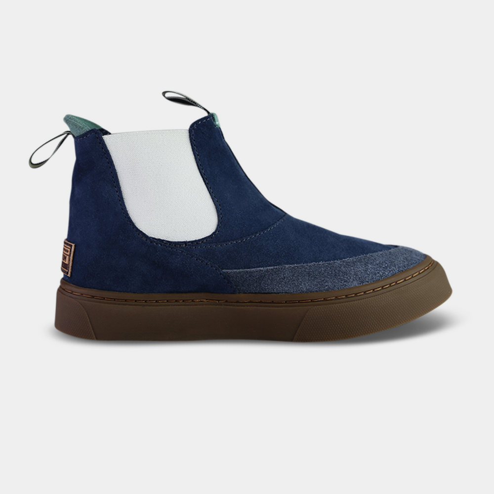 
                      
                        Side shot, A pair of dark blue suede ankle boots with a brown rubber sole. The boots feature a light brown leather logo tag with "DEVIUM" written on the back of each heel, a mint green elasticated panel, and a black and white striped pull tab at the back of the ankle.
                      
                    