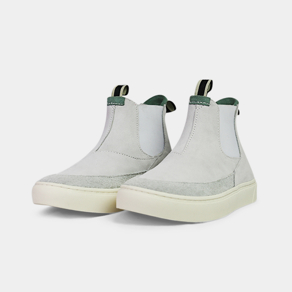 
                      
                        A pair of white suede boots with white soles. The boots feature a mint green elasticated panel and a striped brown and black pull tab at the back of the ankle. The toe area is a different texture of suede with a visible seam.
                      
                    