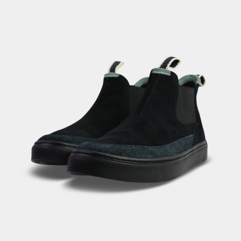 
                      
                        A pair of dark black suede ankle boots with a brown rubber sole. The boots feature a light brown leather logo tag with "DEVium" written on the back of each heel, a mint green elasticated panel, and a black and white striped pull tab at the back of the ankle.
                      
                    