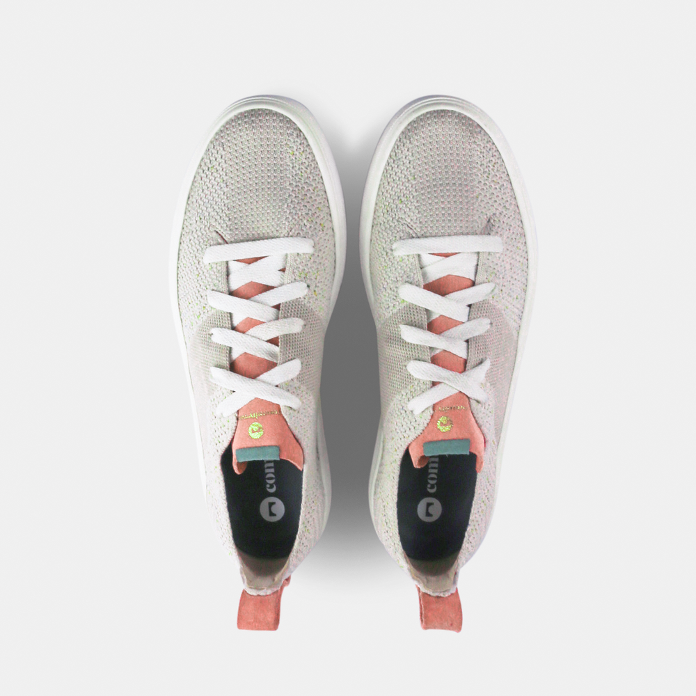 
                      
                        A pair of off-white knitted sneakers with light pink speckles. The shoes have white laces, a pale pink tongue, and a pink and white heel loop. The insoles are dark green with a white text logo and a circle.
                      
                    