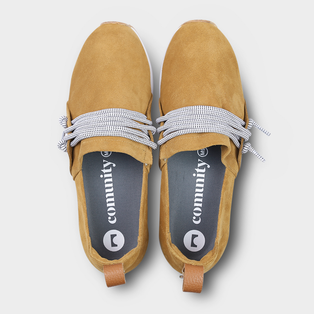 
                      
                        Mateos, A high-angle, top-down product shot of a pair of brown suede slip-on shoes. The shoes have thick, speckled black and white rope-like laces that are tied in a loose knot across the top of the foot. The insoles are dark gray with the word "comunity" and a circular logo printed on them in white. The shoes have a small brown leather loop on the heel. The background is a solid light gray.
                      
                    
