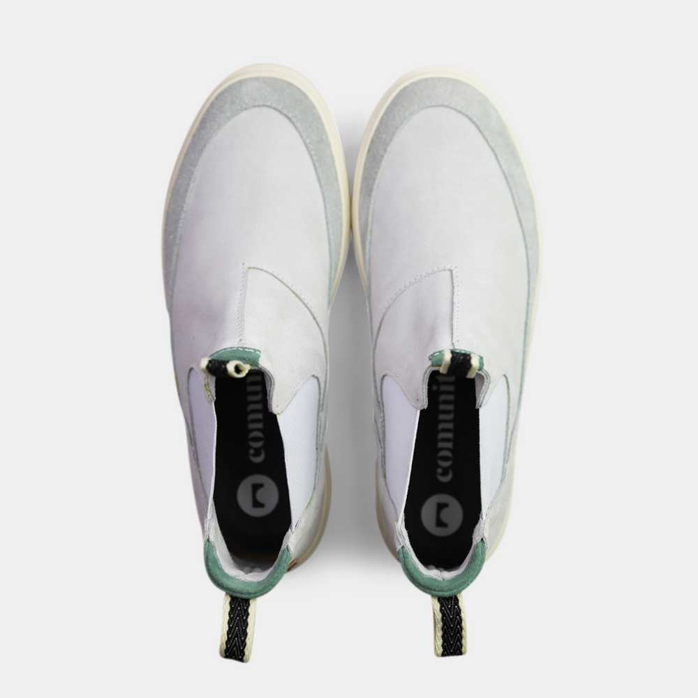 
                      
                        A pair of white suede boots with white soles. The boots feature a mint green elasticated panel and a striped brown and black pull tab at the back of the ankle. The toe area is a different texture of suede with a visible seam.
                      
                    