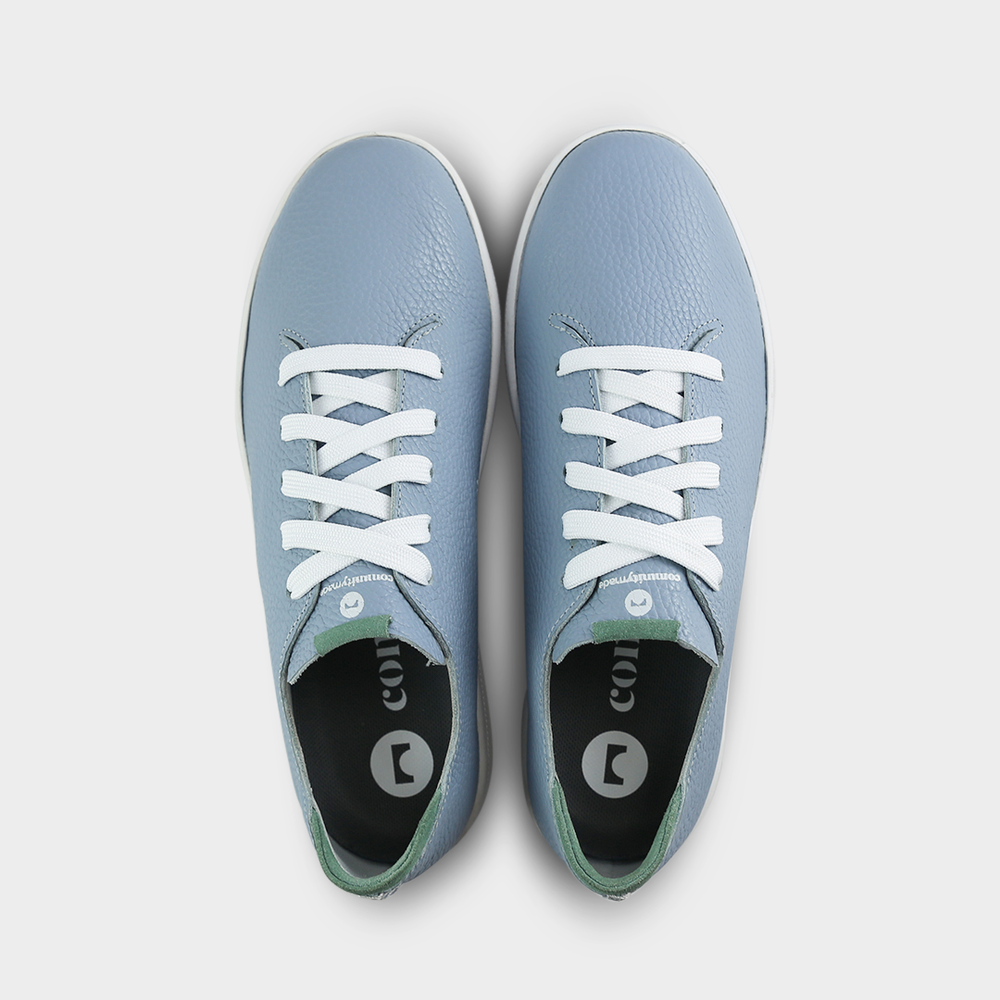 
                      
                        A top view shot of pair of sky blue leather sneakers with a lace-up closure featuring flat white shoelaces, white printing on the tongue and a dark grey sockliner with a circle logo and COMUNITY printed in white with a green heel accent.
                      
                    