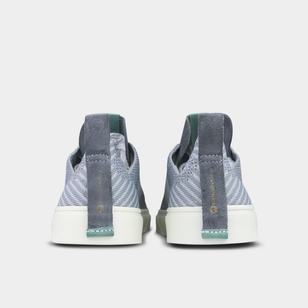 
                      
                        A pair of light gray knitted sneakers. The shoes have a thick, gray suede pull tab on the back with a gold logo and a small mint green detail at the base.
                      
                    
