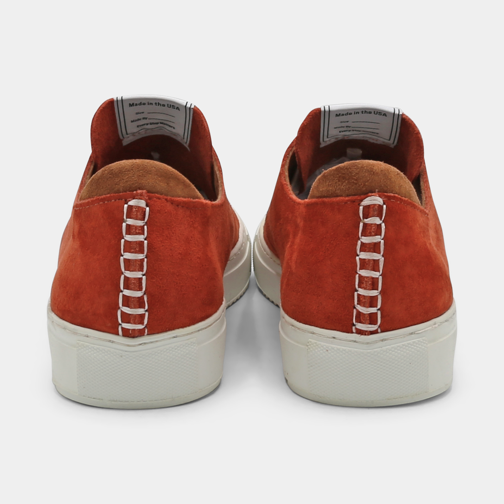 
                      
                        A rust colored low-top sneaker with a white sole and laces, back view.
                      
                    