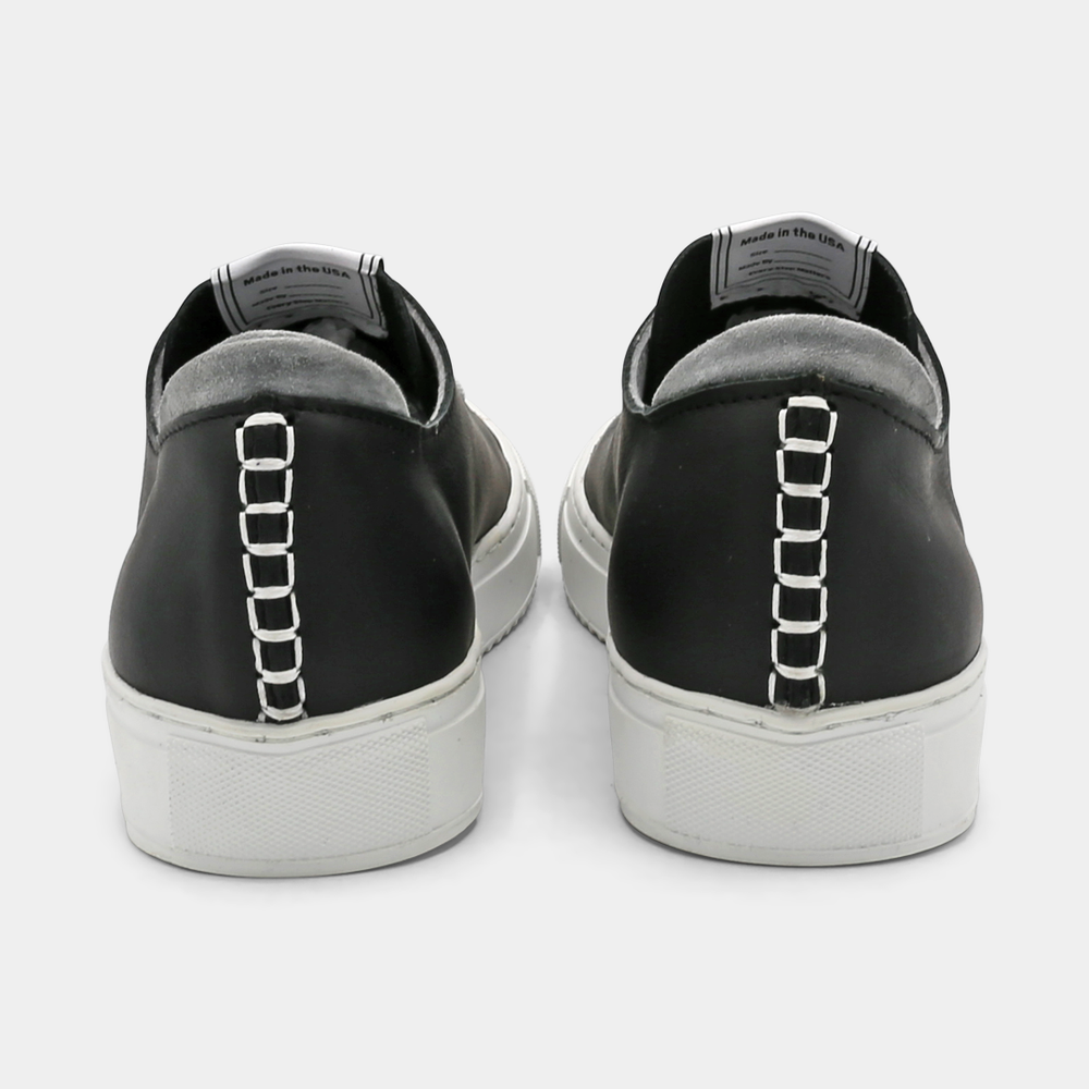 
                      
                        A black colored low-top sneaker with a white sole and laces, back view.
                      
                    