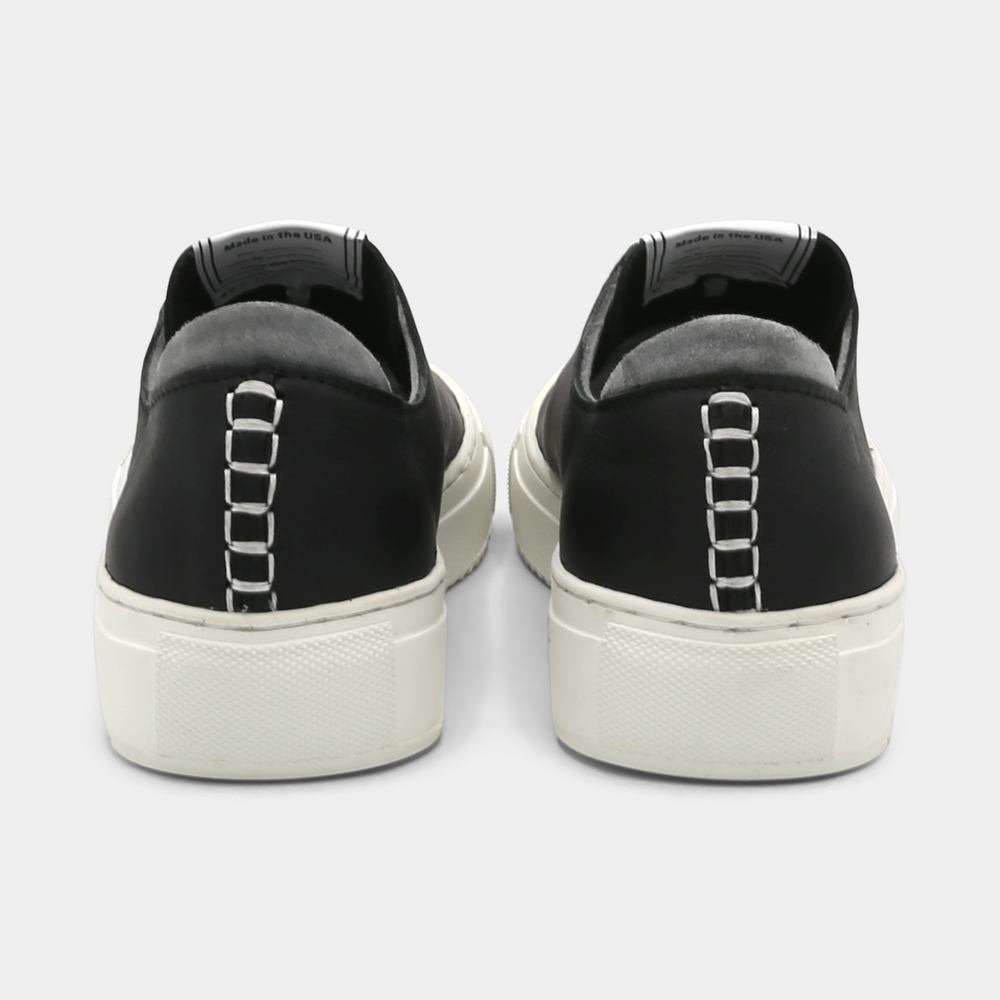 
                      
                        A black colored low-top sneaker with a white sole and laces, back view.
                      
                    