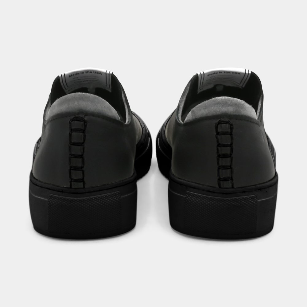 
                      
                        A black colored low-top sneaker with a black sole and laces, back view.
                      
                    