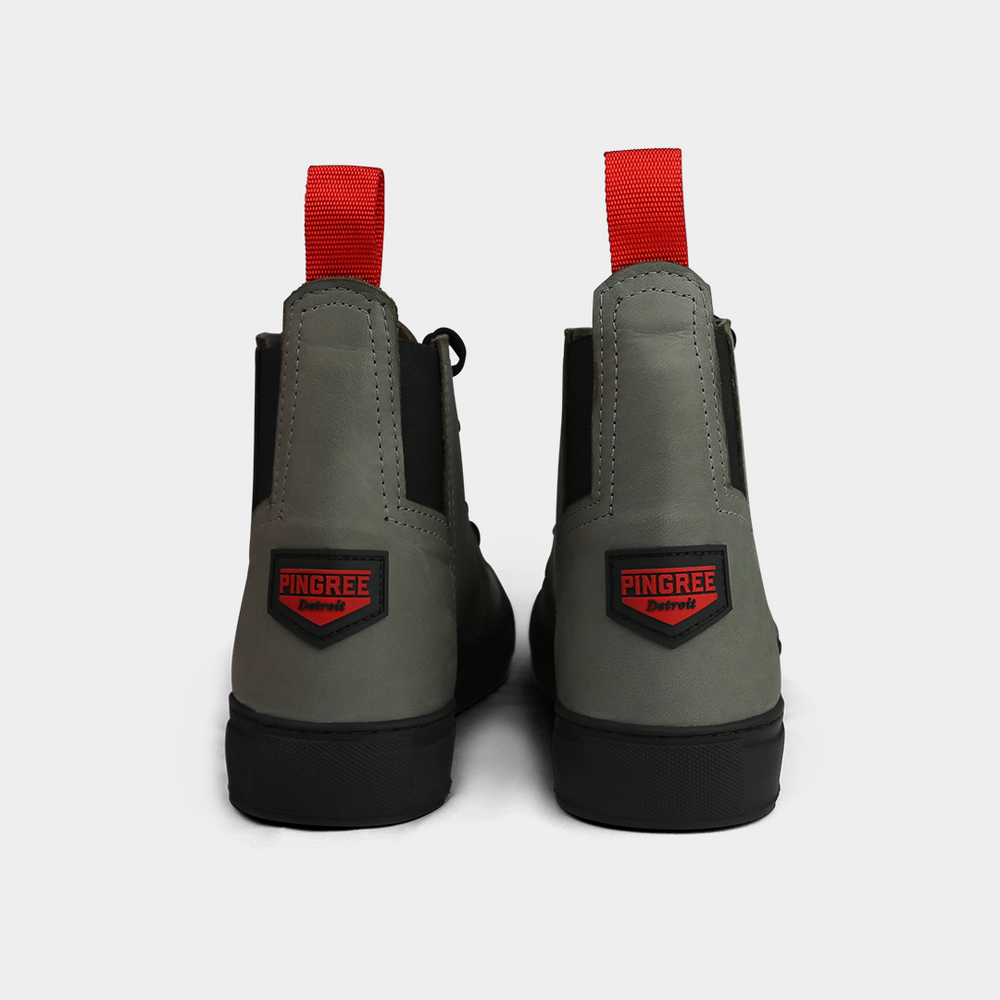 
                      
                        A head-on product shot of the back of a pair of gray high-top shoes. The shoes are made of gray leather, with a thick black sole and a red loop on the back of the ankle. A red and black shield-shaped patch with "PINGREE Detroit" written on it is visible on the heel of each shoe. The background is a solid light gray.
                      
                    