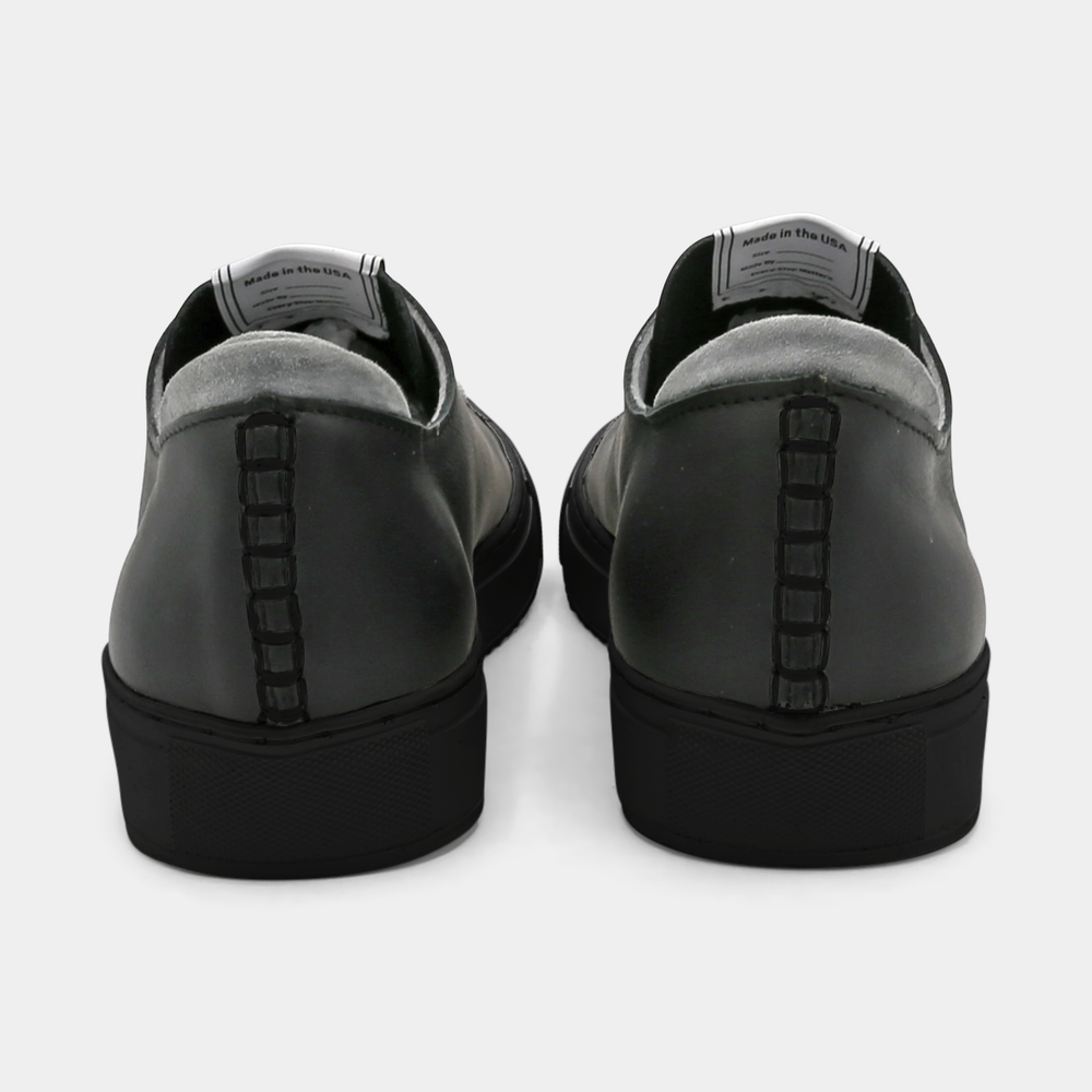 
                      
                        A black colored low-top sneaker with a black sole and laces, back view.
                      
                    