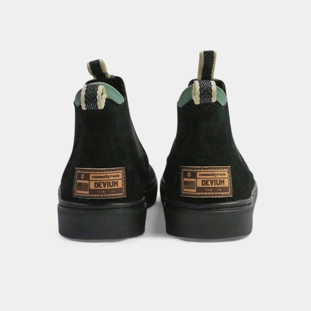 
                      
                        A pair of dark black suede ankle boots with a brown rubber sole. The boots feature a light brown leather logo tag with "DEVium" written on the back of each heel, a mint green elasticated panel, and a black and white striped pull tab at the back of the ankle.
                      
                    