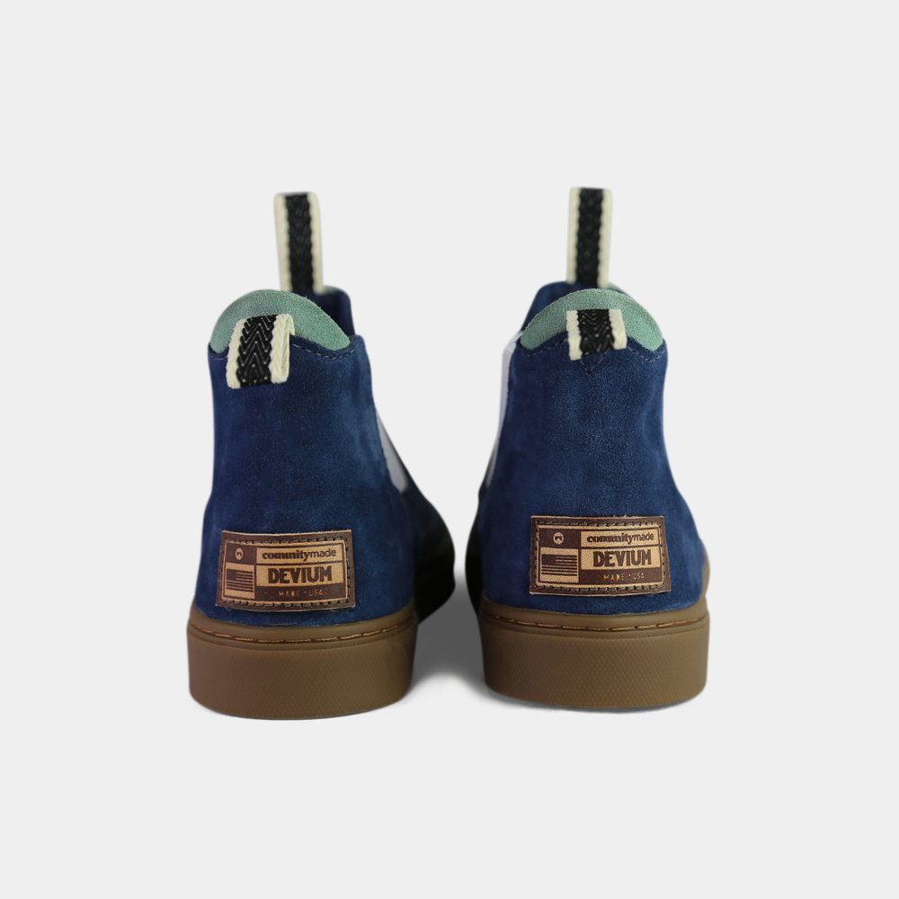 
                      
                        A pair of dark blue suede ankle boots with a brown rubber sole. The boots feature a light brown leather logo tag with "DEVIUM" written on the back of each heel, a mint green elasticated panel, and a black and white striped pull tab at the back of the ankle.
                      
                    