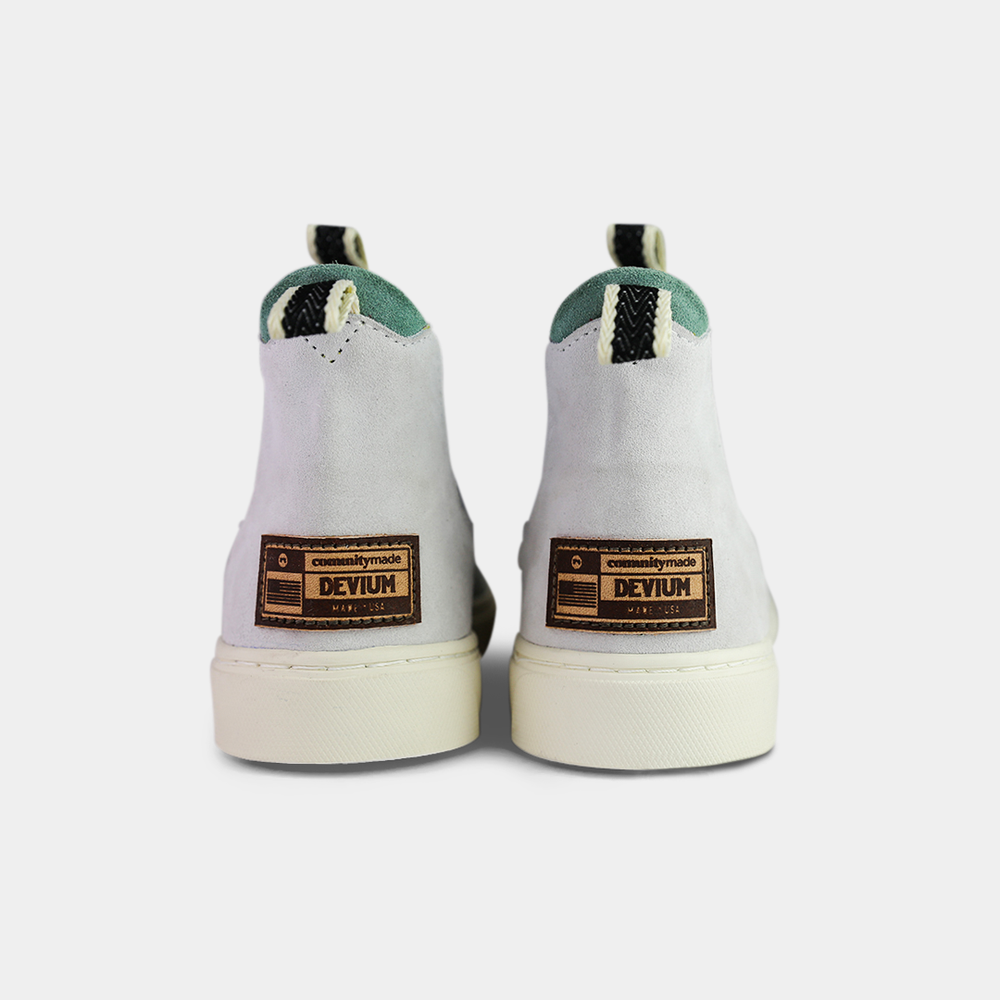 
                      
                        A pair of off-white suede ankle boots with an off-white sole. The boots feature a light brown leather logo tag on the back of each heel, a mint green elasticated panel, and a black and white striped pull tab at the back of the ankle.
                      
                    