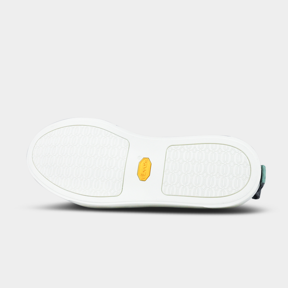 
                      
                        The bottom of a shoe with a white rubber sole. The front and back of the sole have a repeating, circular pattern for grip, with a bright yellow oval logo in the center. A small dark green piece of material is visible at the heel
                      
                    