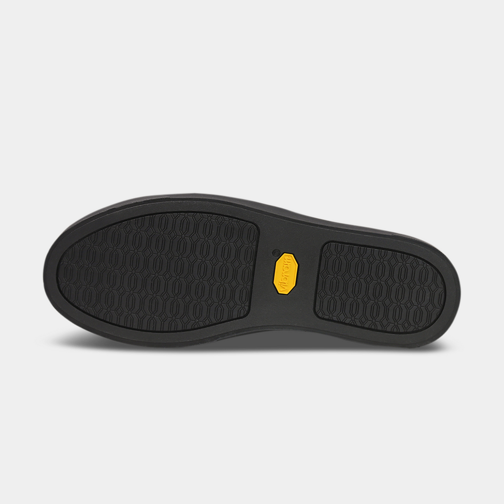 
                      
                        The bottom of a shoe with a black rubber sole. The front and back of the sole have a repeating, circular pattern for grip, with a bright yellow oval logo in the center.
                      
                    