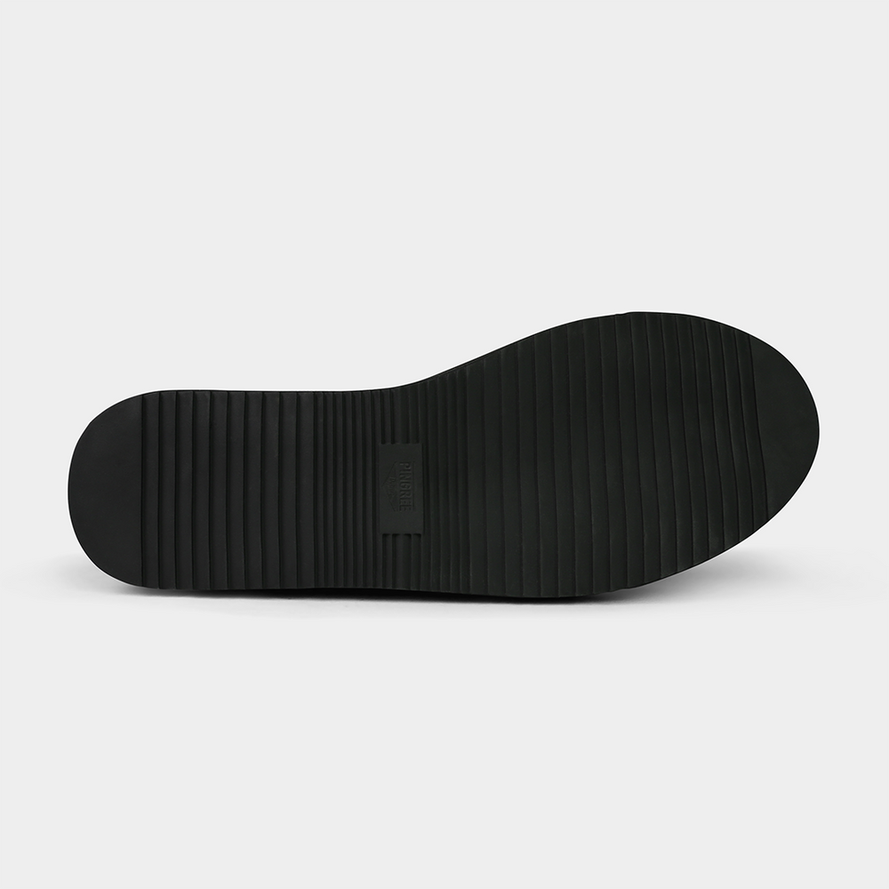 
                      
                        The sole is a solid black with a simple ridged or corrugated tread pattern. A rectangular patch with the word "PINGREE" on it is visible in the middle of the sole. The shoe is on a solid gray background.
                      
                    