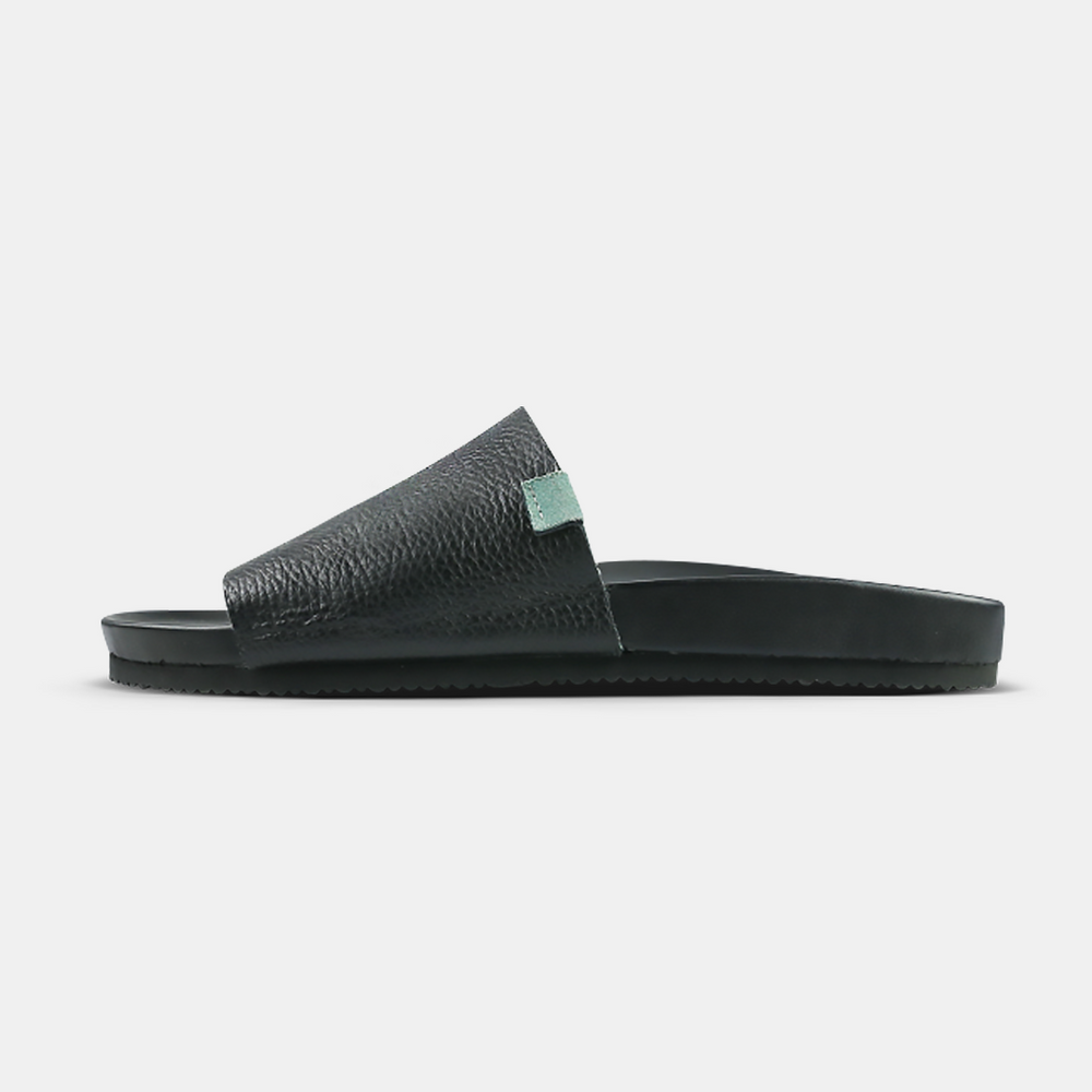 A black leather slide with a contoured cushioned footbed and a Vibram outsole, designed and handcrafted in Los Angeles.