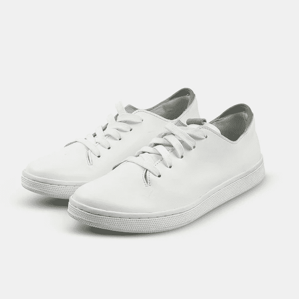 
                      
                        A quarter angle shot of pair of white leather sneakers with a lace-up closure featuring flat white shoelaces, a white rubber cupsole and a green accent on the heel.
                      
                    